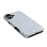 Merrigold iPhone case featuring a light blue floral pattern with white and yellow accents, angled view showing camera cutout.