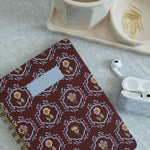 Merrigold notebook with floral design, gold spiral binding, placed on a marble surface with a cup and stationery.