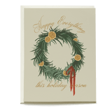 Orange wreath holiday card featuring dried orange slices, green pine branches, and a red ribbon with gold text.