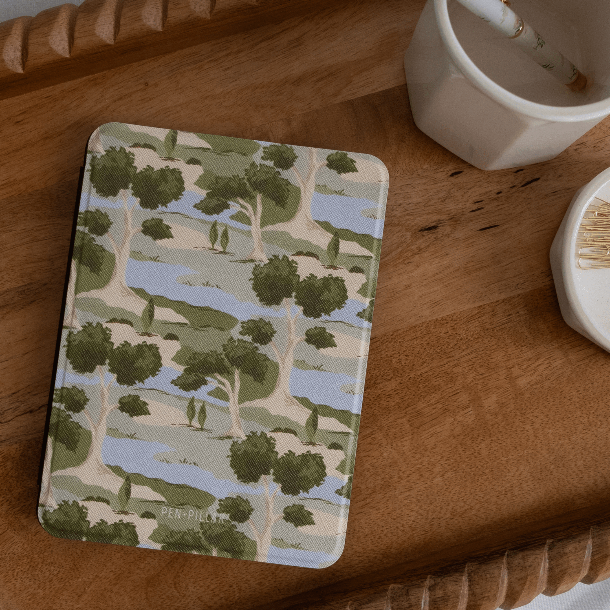 Orchard Kindle case featuring a green and beige tree pattern on a textured background, placed on a wooden surface.