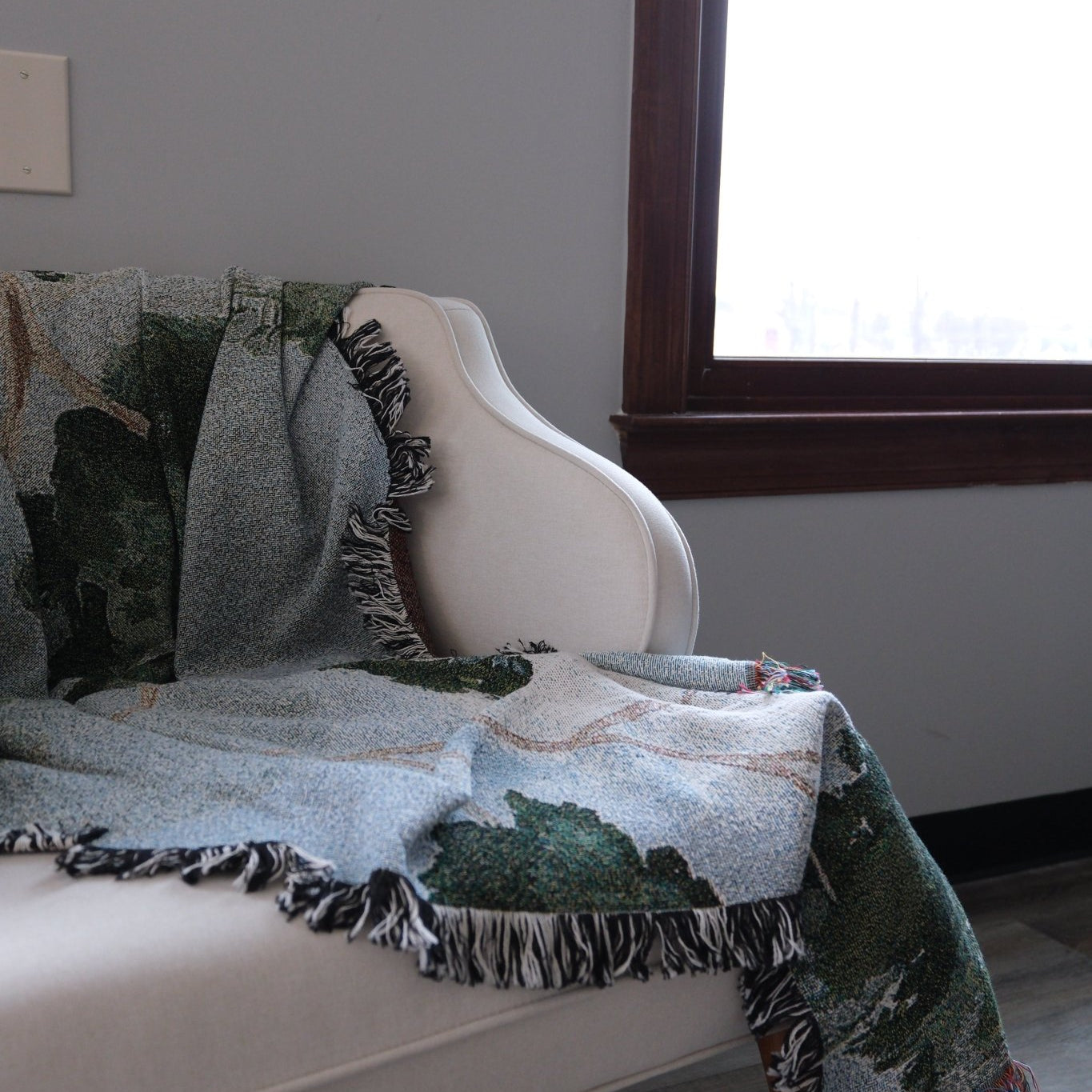 Orchard woven blanket draped over a light-colored chair, featuring green and blue patterns with fringed edges.