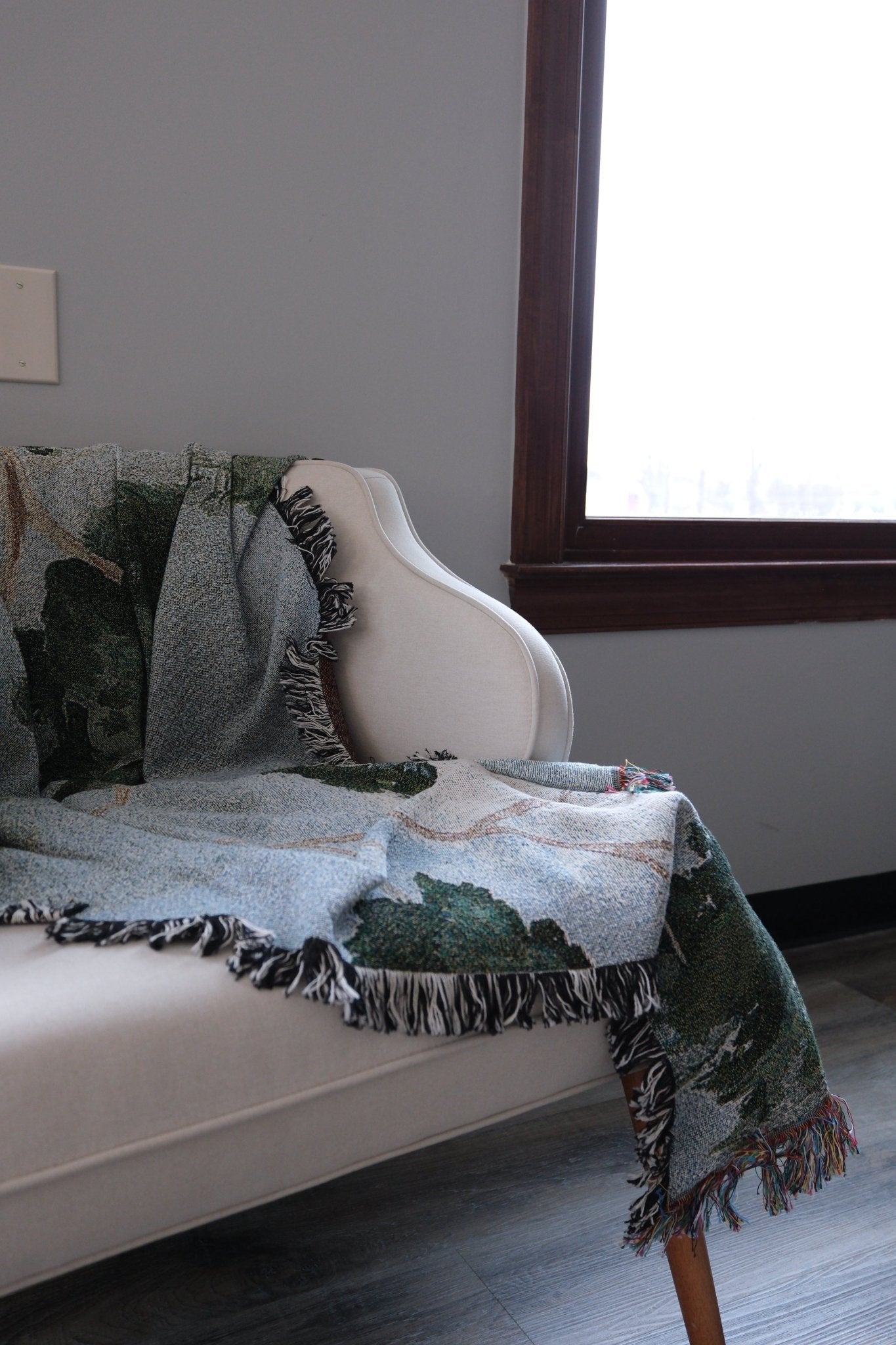 Orchard woven blanket draped over a light-colored chair, featuring green and blue patterns with fringed edges.