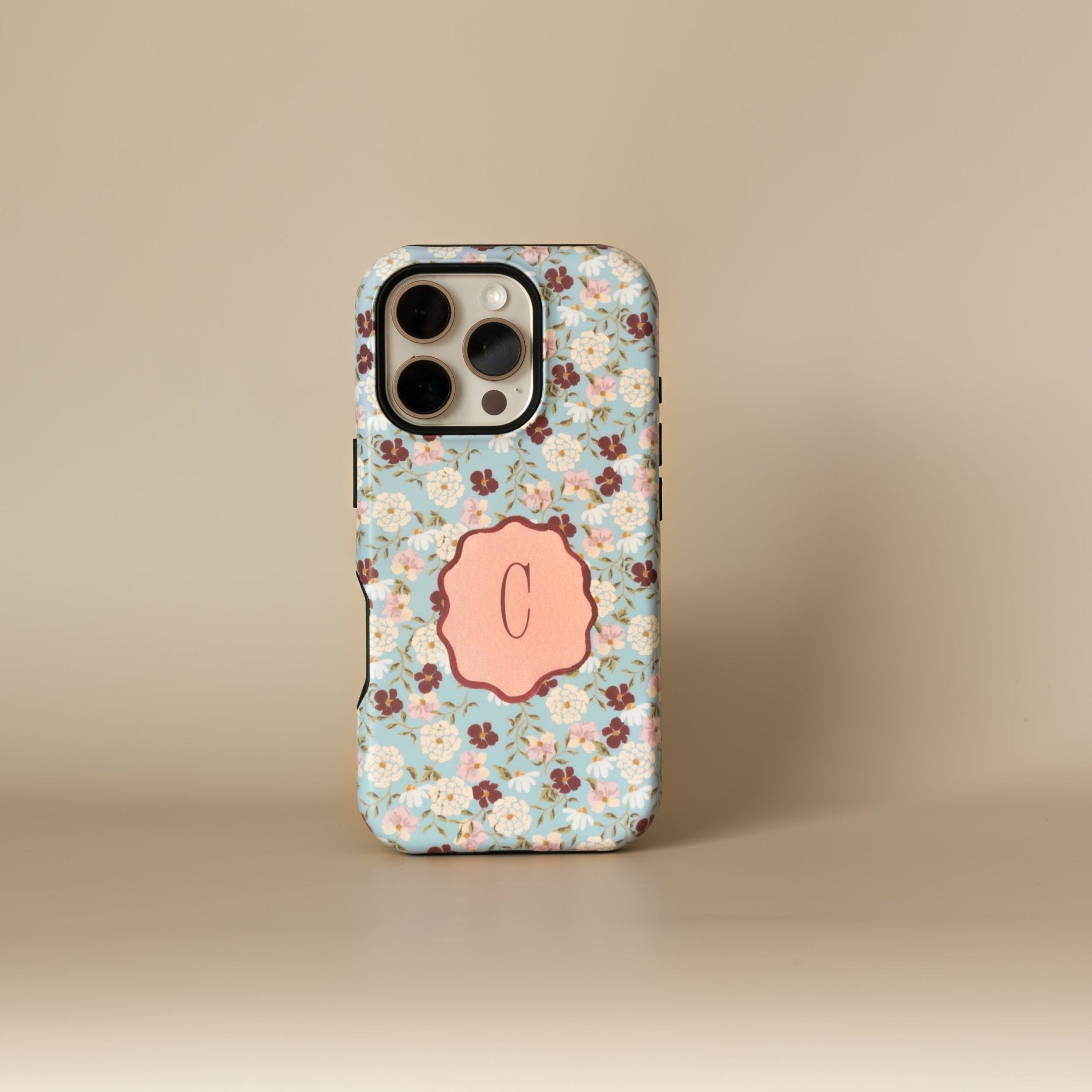 Personalized iPhone case with a floral pattern in blue, featuring a pink monogrammed initial "C" on the back.