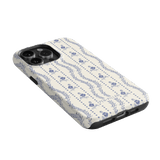Riviera iPhone case featuring a floral pattern in blue on a cream background, angled to show the camera cutout.