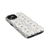 Riviera iPhone case featuring a floral pattern in blue on a cream background, angled to show the side and camera cutout.