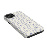 Riviera iPhone case featuring a floral pattern in blue on a cream background, angled to show the camera cutout.