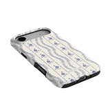 Riviera iPhone case featuring a floral pattern in blue on a cream background, angled view showing buttons and ports.