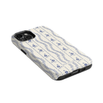 Riviera iPhone case featuring a floral pattern in blue on a cream background, angled view showing ports and buttons.