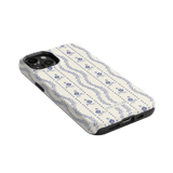 Riviera iPhone case featuring a floral pattern in blue on a cream background, angled view showing ports and buttons.