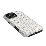 Riviera iPhone case featuring a floral pattern in blue on a cream background, angled to show the camera cutout.