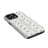 Riviera iPhone case featuring a floral pattern in blue on a cream background, angled to show the camera cutout.