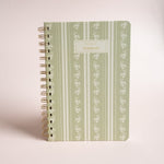 Roselle notebook with a green floral design and gold spiral binding on a light background.