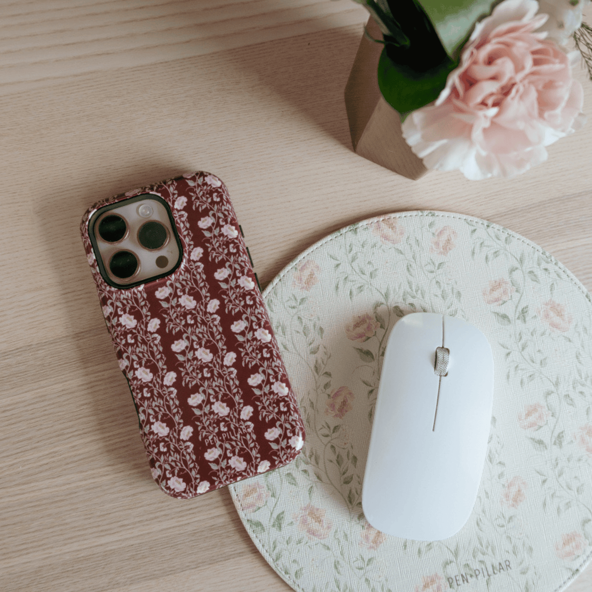 Thicket iPhone case on a floral desk mat beside a white mouse and pink carnations