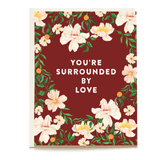 Sympathy card with floral design and the text "You're surrounded by love" on a burgundy background.