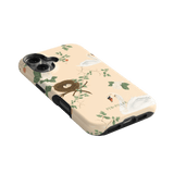 Swan Hollow iPhone case featuring swan illustrations, a nest, and green foliage on a soft peach background.
