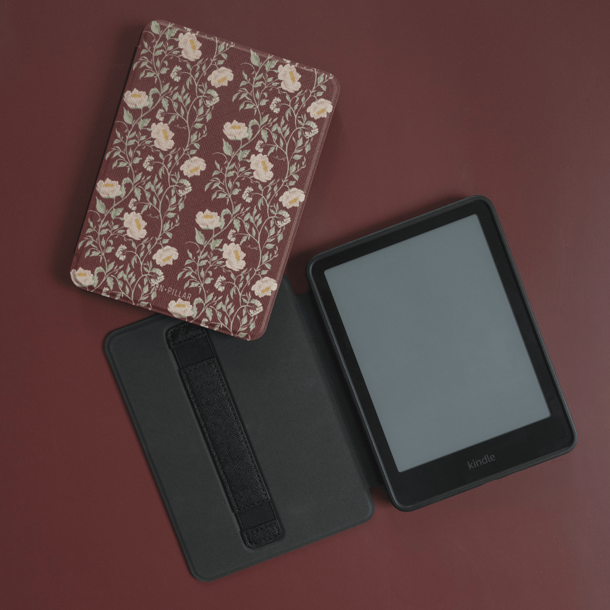 Thicket Kindle case with floral design, open beside a black Kindle device on a maroon background.