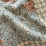 Thicket woven blanket featuring a floral pattern on a blue background with a checkered beige border.
