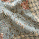 Thicket woven blanket featuring a floral pattern on a blue background with a checkered beige border.