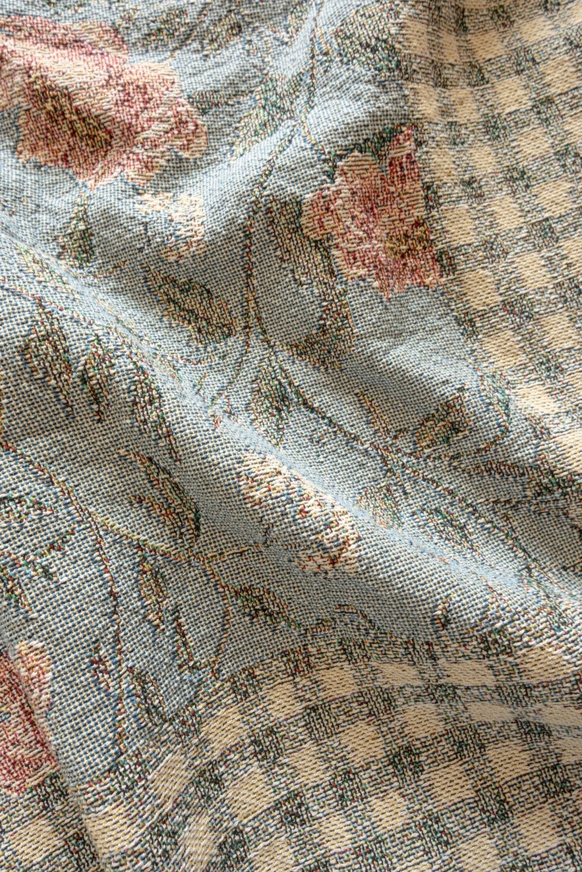 Thicket woven blanket featuring a floral pattern on a blue background with a checkered beige border.