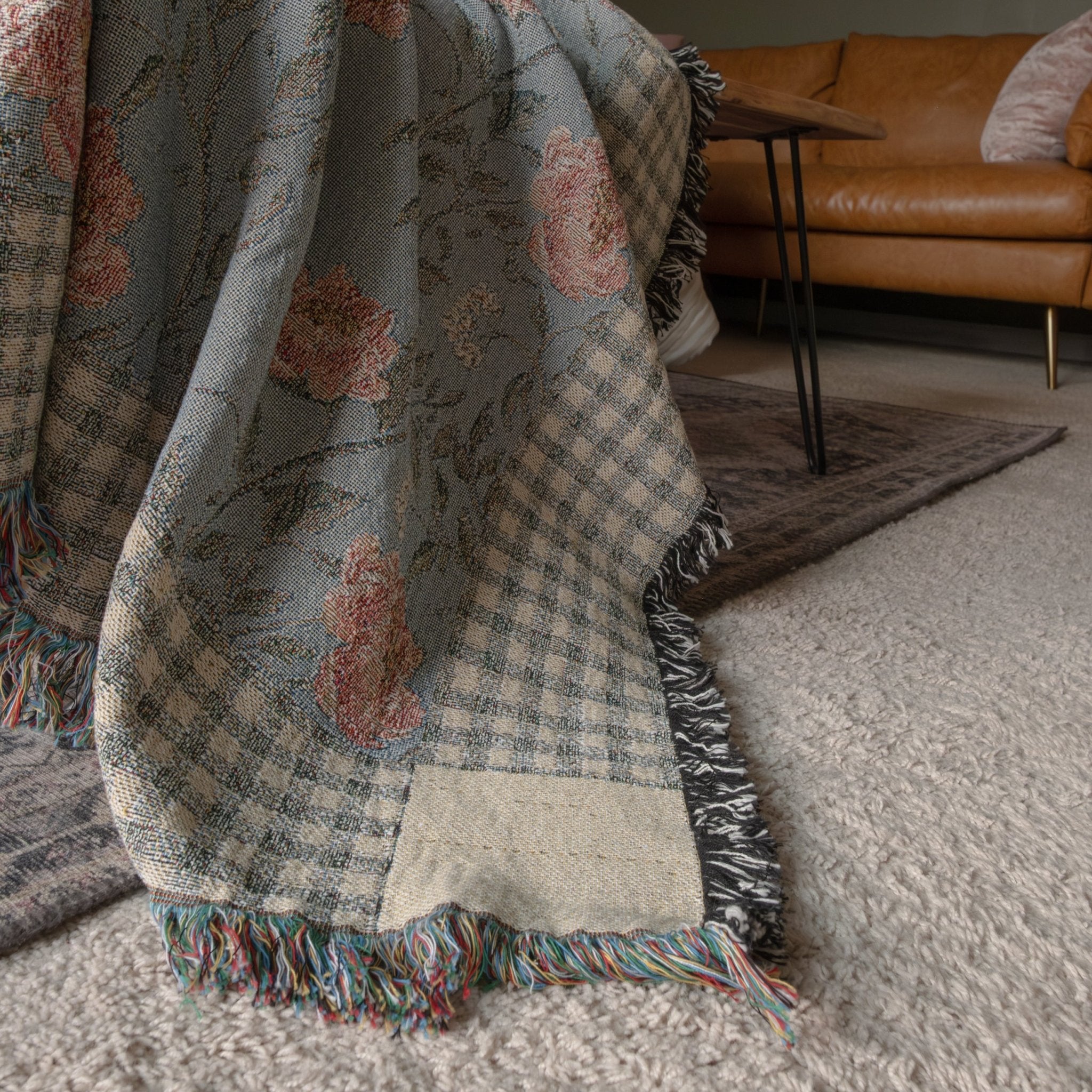 Thicket woven blanket featuring a floral pattern in blue and pink, with fringed edges on a textured surface.