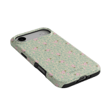 Vine+Bloom iPhone case featuring a green floral pattern with pink flowers, angled view showing buttons and ports.