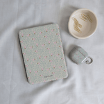 Vine+Bloom Kindle case with a floral pattern in pastel colors, placed on a light fabric surface alongside paper clips.