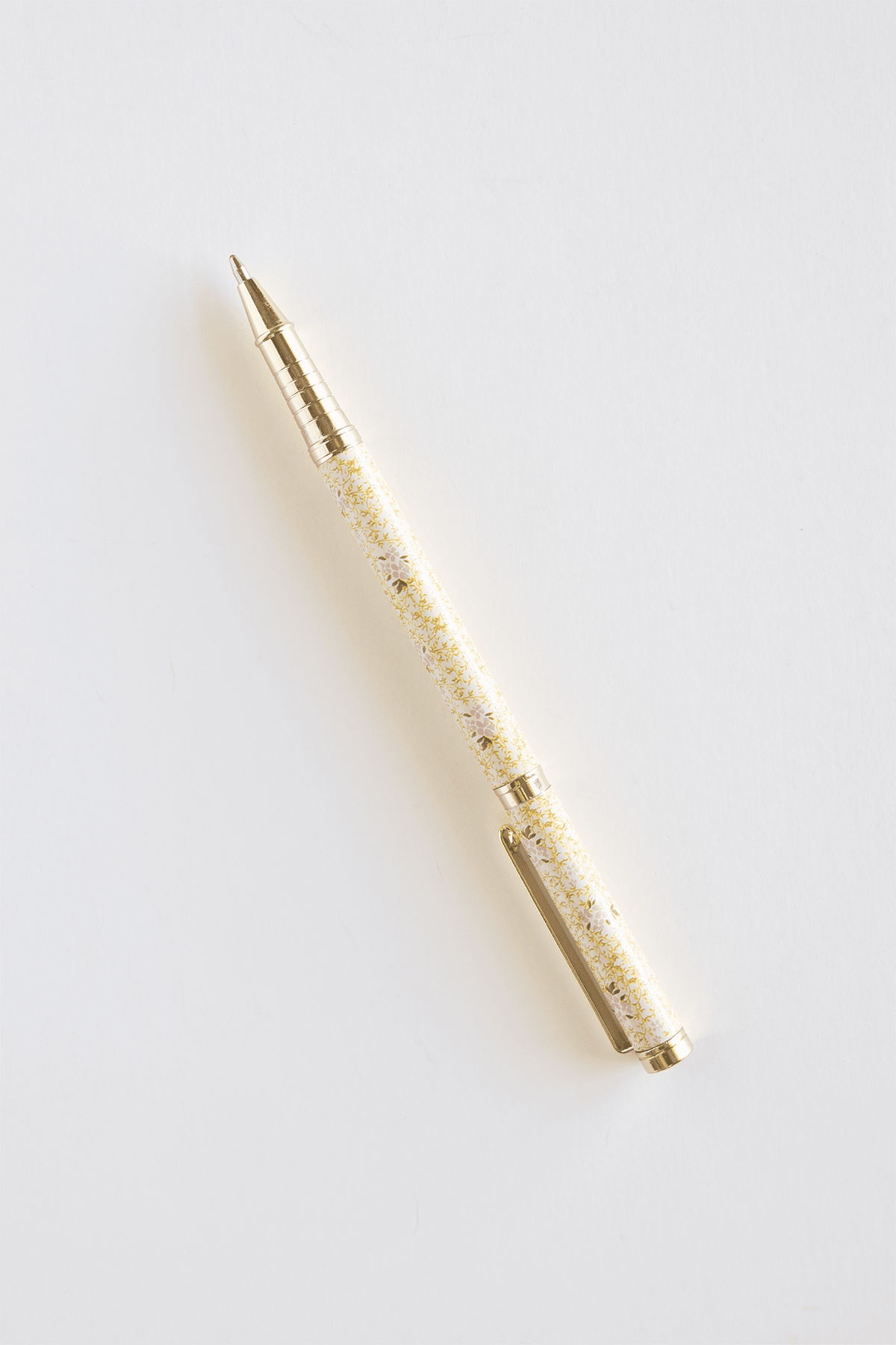 Vine+Bloom metal pen with a gold and white floral design, featuring a retractable tip and clip for easy carrying.