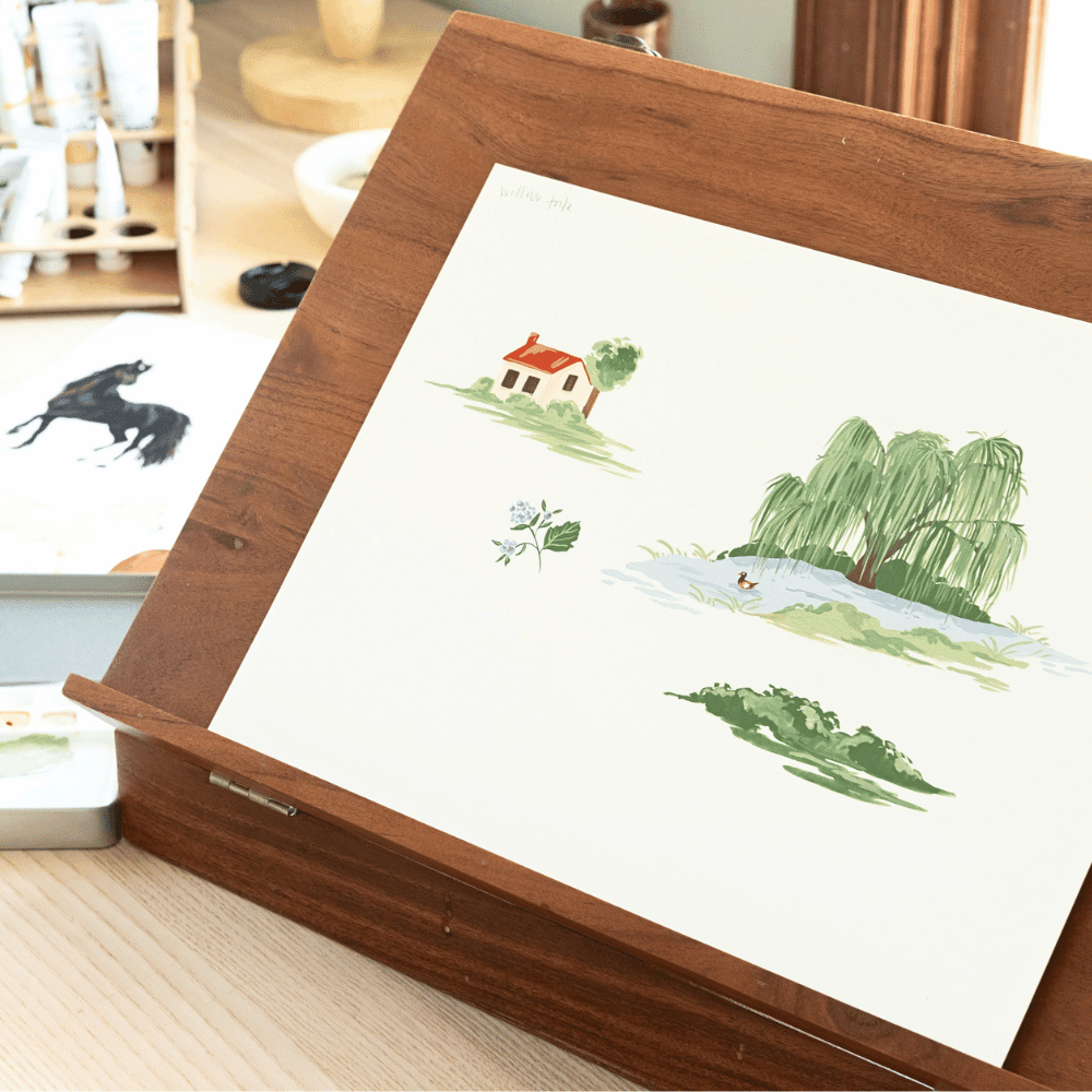 White Willow iPhone Case on a wooden easel featuring illustrations of a cottage, willow tree, and flowers.